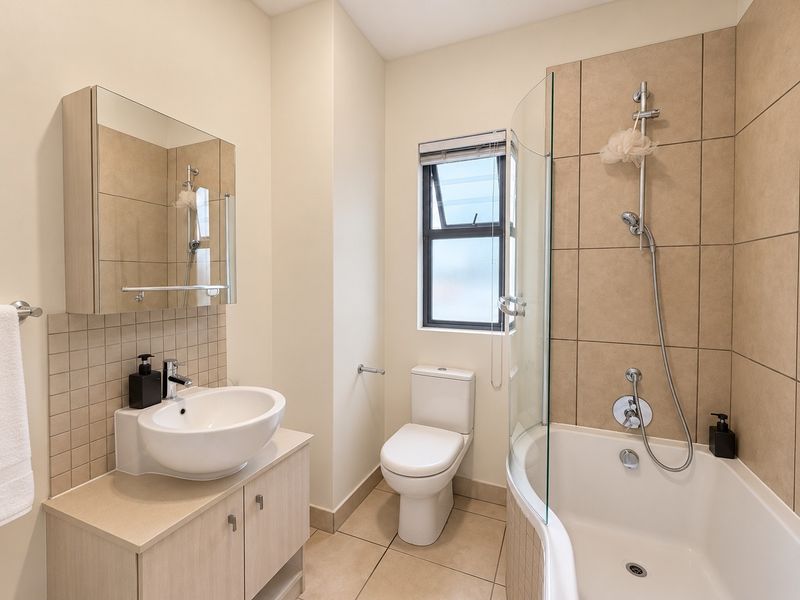 A well-maintained bathroom featuring a vanity with vessel sink, mirrored cabinet, toilet, and a shower-over-bath combination with a glass screen.