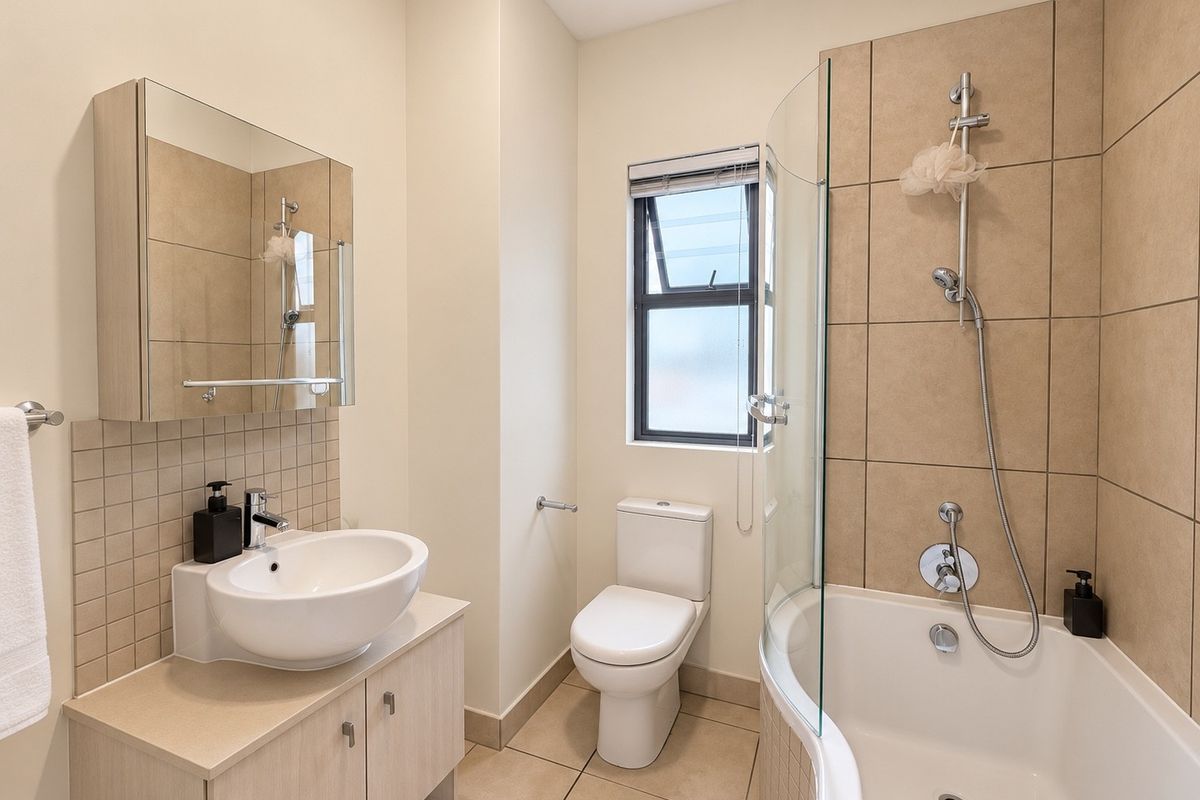 A well-maintained bathroom featuring a vanity with vessel sink, mirrored cabinet, toilet, and a shower-over-bath combination with a glass screen.
