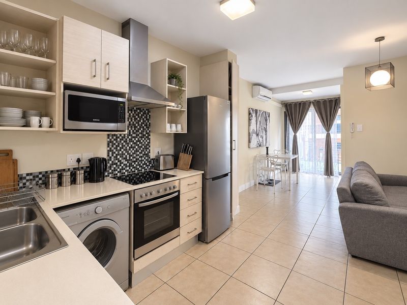 Modern open-plan kitchen and living area featuring tiled floors, built-in cabinetry, integrated appliances, and direct access to a balcony through sliding glass doors.