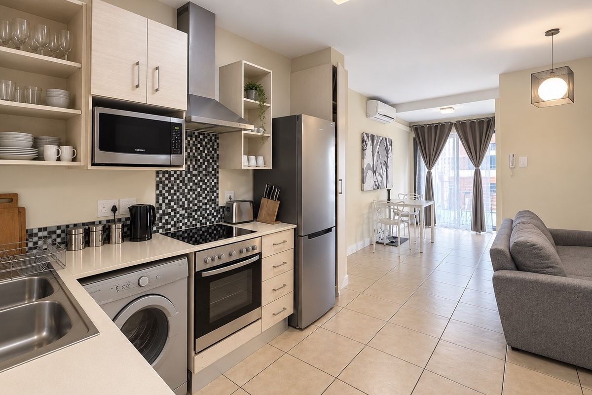 Modern open-plan kitchen and living area featuring tiled floors, built-in cabinetry, integrated appliances, and direct access to a balcony through sliding glass doors.
