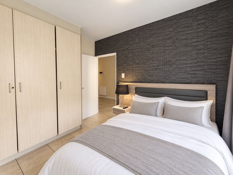 A well-maintained bedroom featuring modern built-in cupboards, tiled flooring, and a stylish textured feature wall with an integrated headboard.