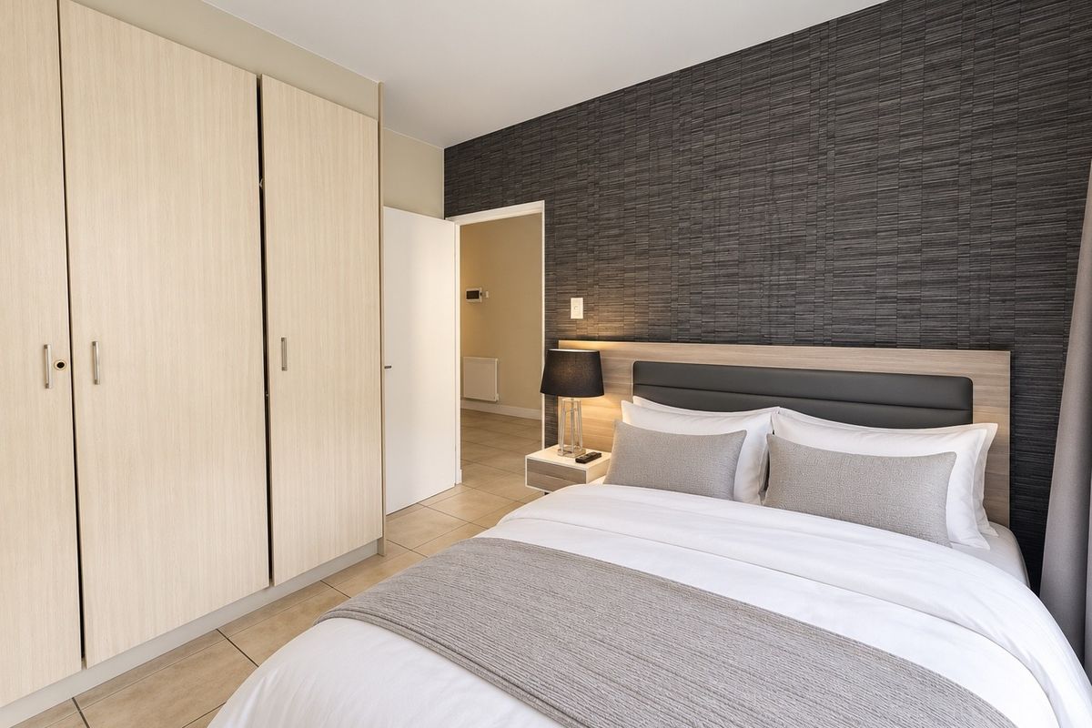 A well-maintained bedroom featuring modern built-in cupboards, tiled flooring, and a stylish textured feature wall with an integrated headboard.