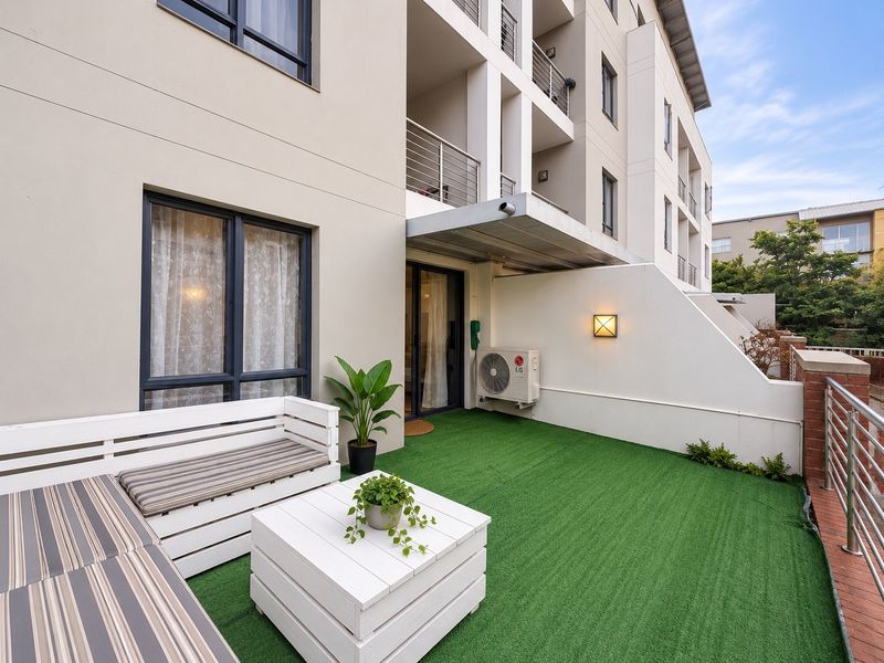 A well-maintained ground floor patio featuring artificial turf, modern metal balustrades, and an integrated air conditioning unit, providing a clean outdoor living space.