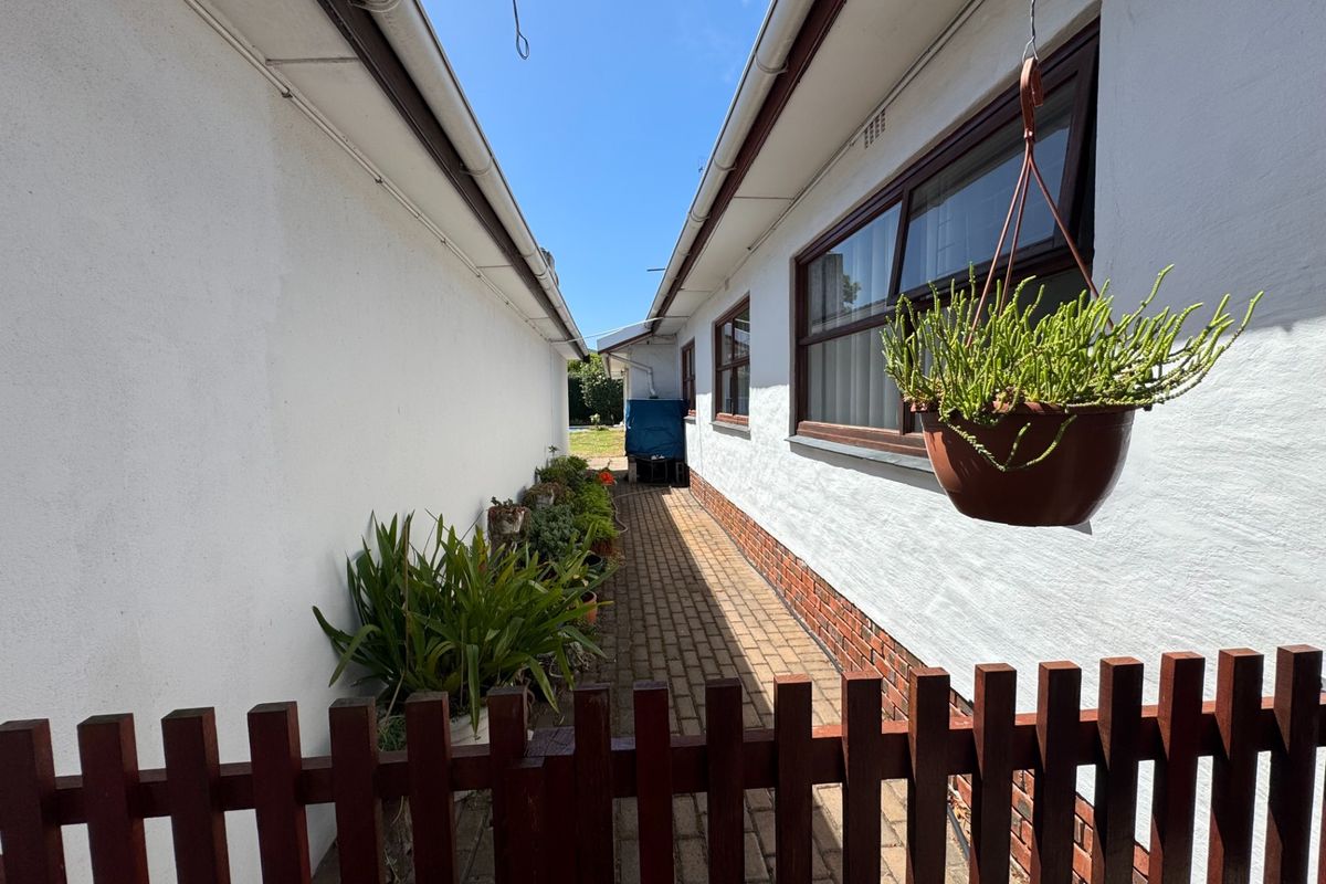 A narrow side passage featuring brick paving, white rendered walls, and a timber fence, providing access to the rear garden area.