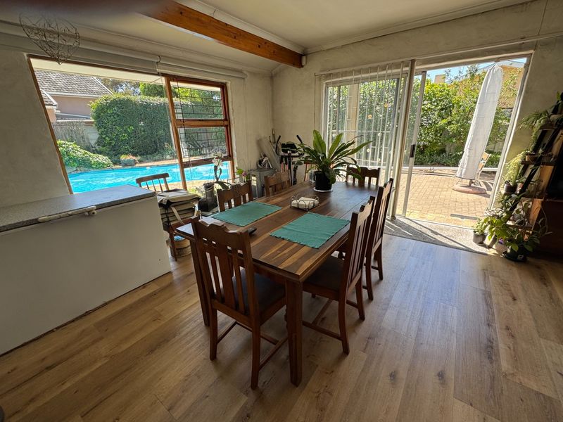 Dining room featuring laminate flooring, exposed timber ceiling beams, and large sliding glass doors providing direct access to the pool and patio area.