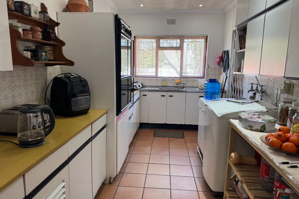 A functional galley-style kitchen featuring built-in cabinetry, a double wall oven, tiled flooring, and a stainless steel sink with a window view.