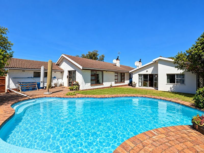 A well-maintained rear garden featuring a swimming pool with brick coping, a paved patio area, and direct access to the house via sliding doors.