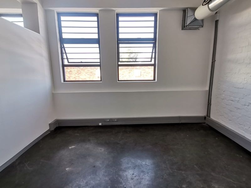 An empty industrial-style office space featuring exposed brick walls, concrete flooring, and functional louvre windows with integrated ventilation ducting.