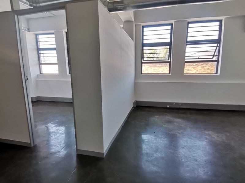 A bright, open-plan office space featuring polished concrete floors, exposed industrial ducting, and large steel-framed windows providing ample natural light.