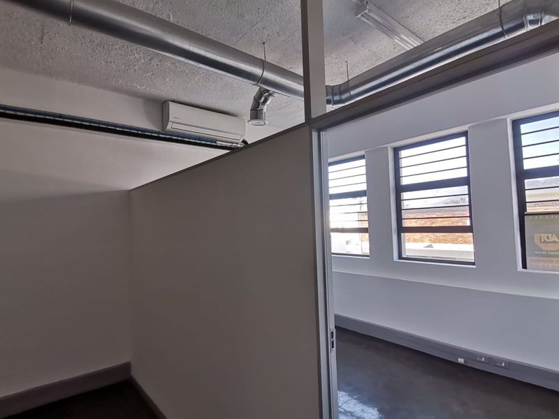 Modern office space featuring exposed industrial ducting, split-system air conditioning, partition walls, and large windows providing ample natural light.