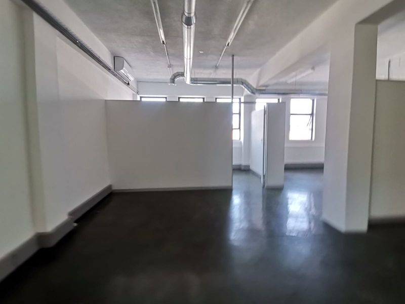 Open plan office space featuring polished concrete floors, exposed industrial ducting, and partition walls, providing a versatile and modern workspace environment.