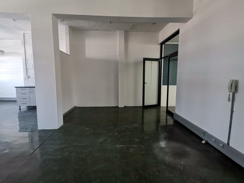 An open-plan office space featuring polished concrete floors, structural columns, and a glass-paneled entrance door, offering a clean and versatile workspace.
