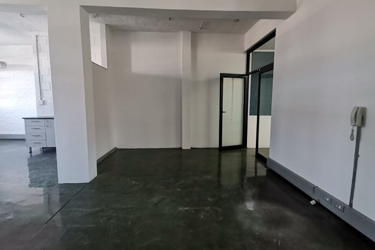 An open-plan office space featuring polished concrete floors, structural columns, and a glass-paneled entrance door, offering a clean and versatile workspace.