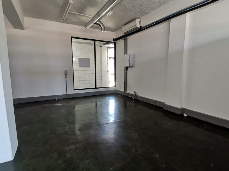 A modern, open-plan office space featuring polished concrete floors, exposed industrial ceiling ducting, and a large glass partition window for natural light.