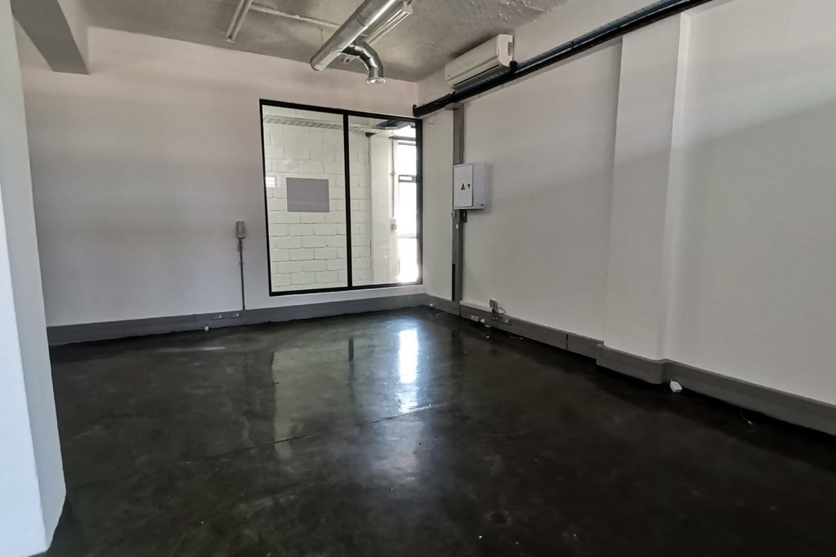 A modern, open-plan office space featuring polished concrete floors, exposed industrial ceiling ducting, and a large glass partition window for natural light.