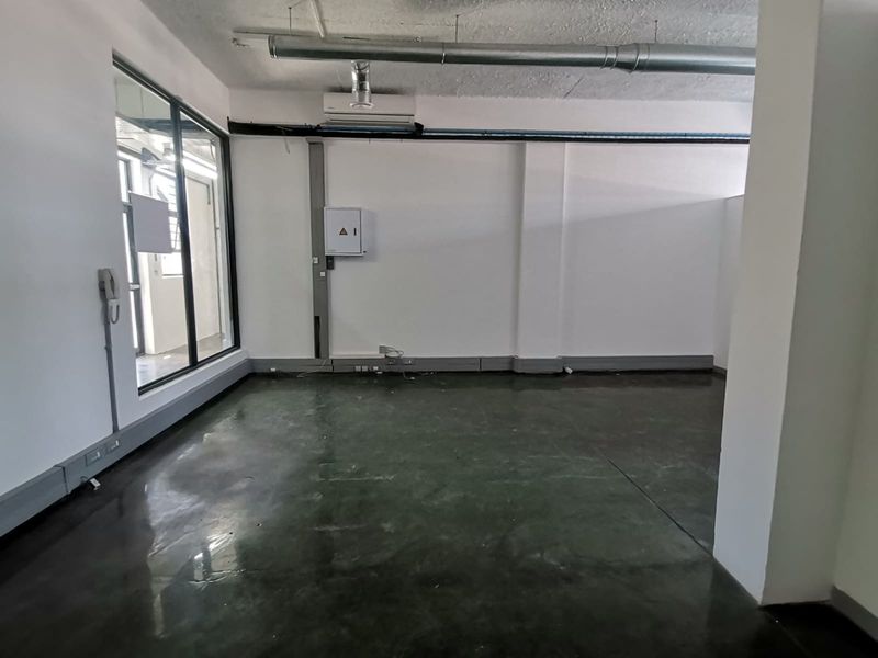 A modern, open-plan office space featuring polished concrete floors, exposed industrial ducting, and a wall-mounted air conditioning unit.