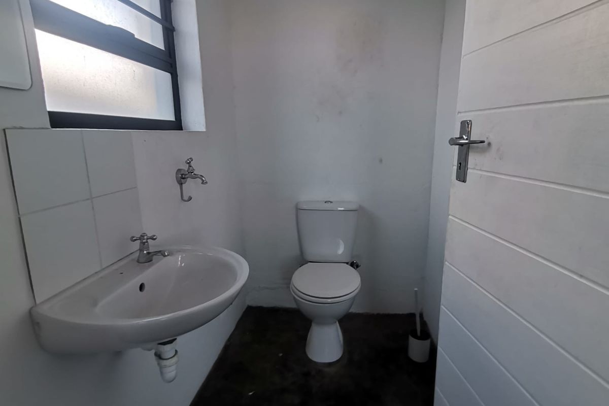 A compact office bathroom featuring a wall-mounted basin and toilet, requiring cosmetic updates to the walls and flooring.