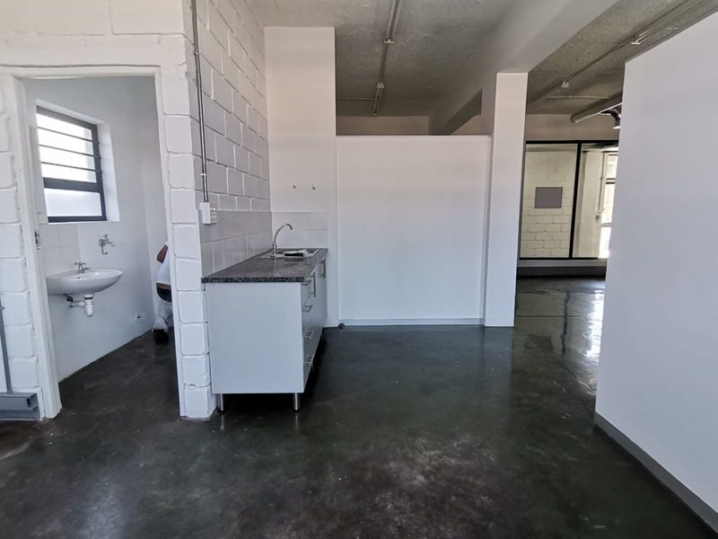 A functional kitchenette area featuring a granite countertop, stainless steel sink, and adjacent basin, set within an industrial-style office space with polished concrete floors.