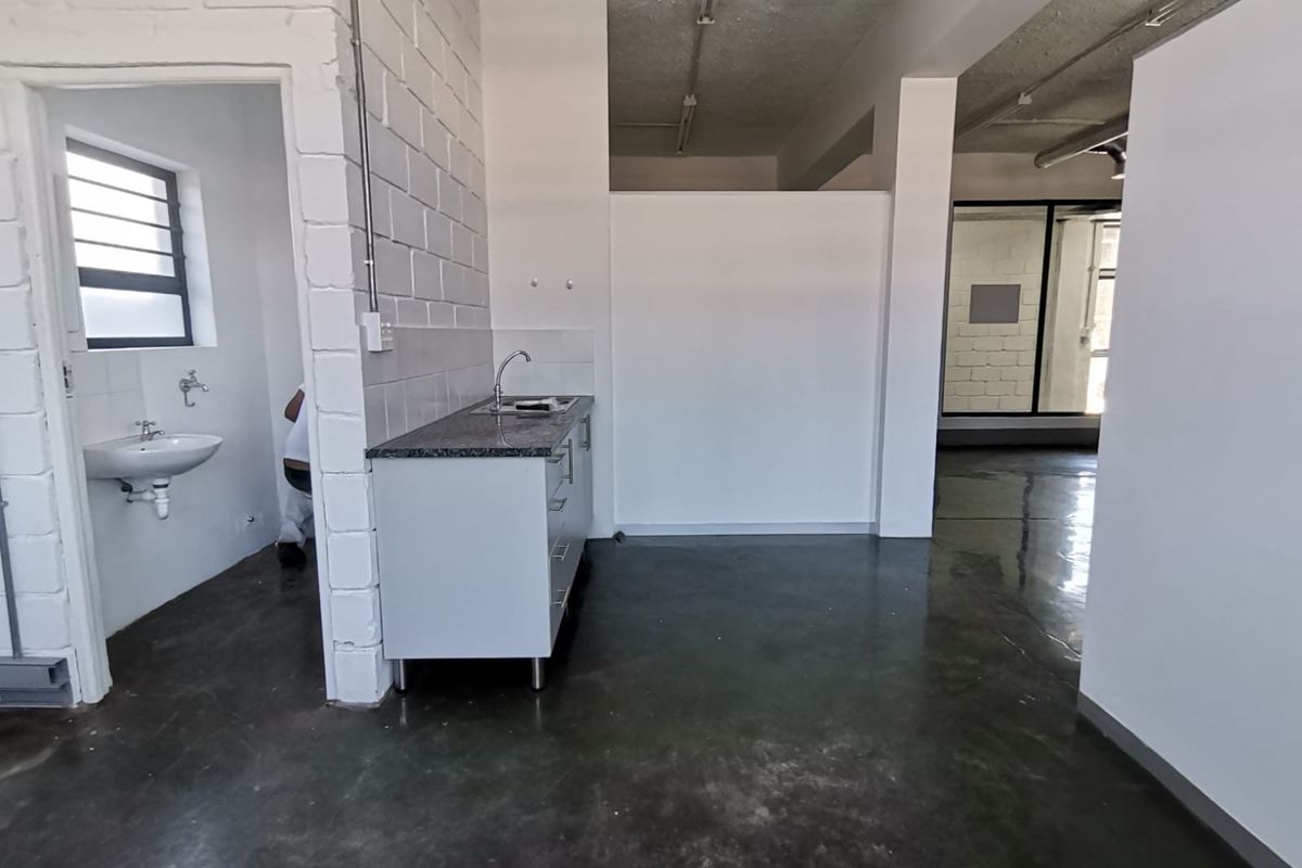 A functional kitchenette area featuring a granite countertop, stainless steel sink, and adjacent basin, set within an industrial-style office space with polished concrete floors.