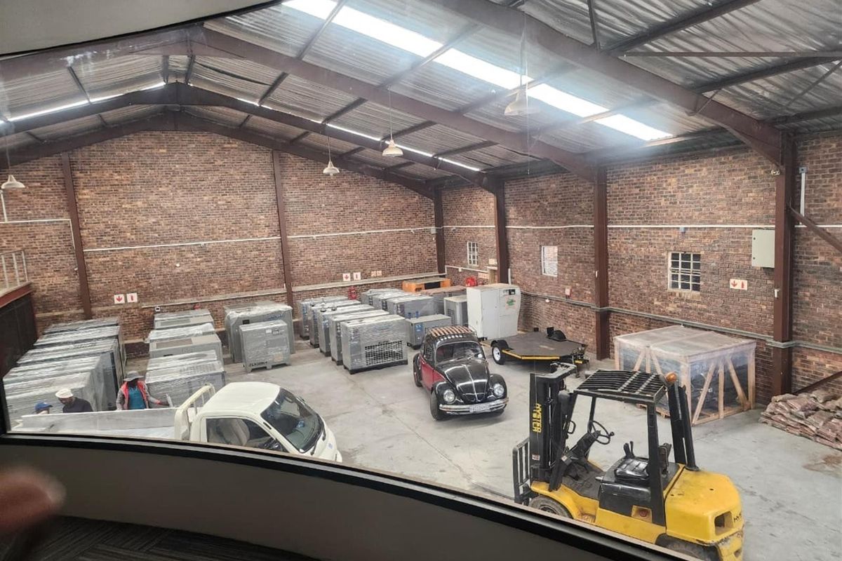 Spacious industrial warehouse featuring exposed brick walls, high steel truss ceilings with integrated skylights, and durable concrete flooring, suitable for storage or manufacturing operations.