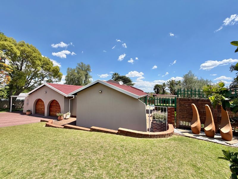 Rear view of the property featuring a well-maintained lawn, brick retaining wall, and a double garage with arched wooden doors under a red roof.