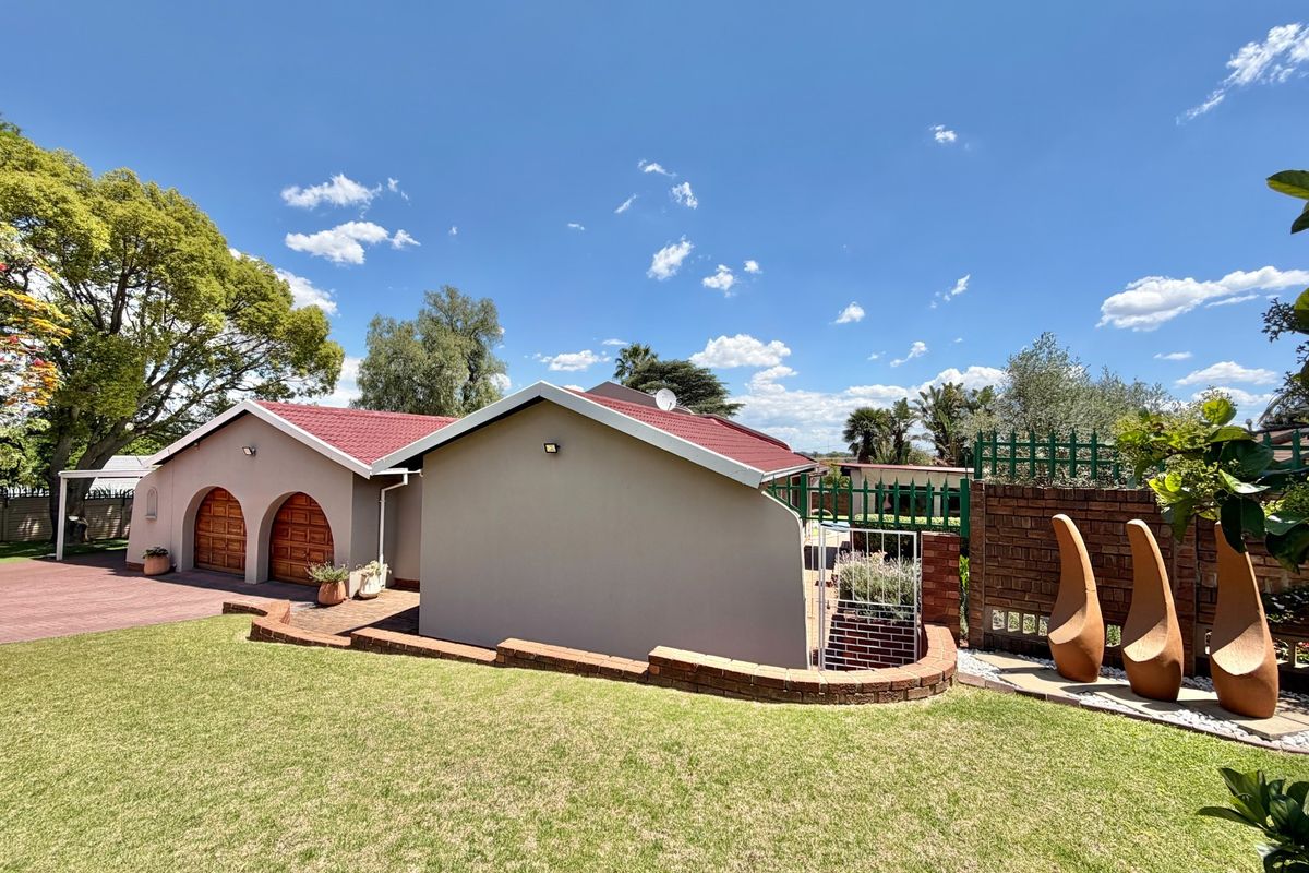 Rear view of the property featuring a well-maintained lawn, brick retaining wall, and a double garage with arched wooden doors under a red roof.