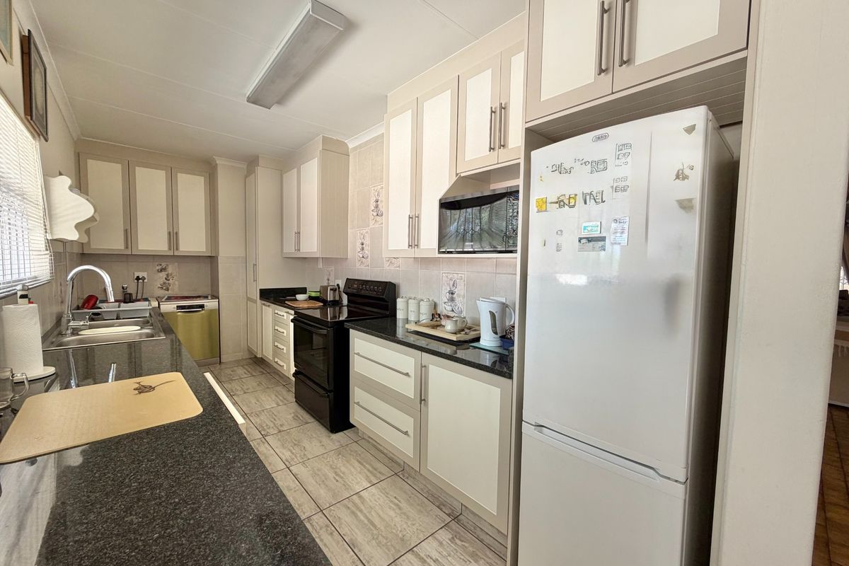 A functional kitchen featuring granite countertops, ample built-in cabinetry, tiled flooring, and a tiled backsplash with integrated stove and extractor fan.
