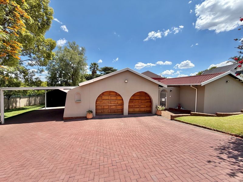 Front elevation of a residential property featuring a double garage with arched wooden doors, a paved driveway, and an attached carport.