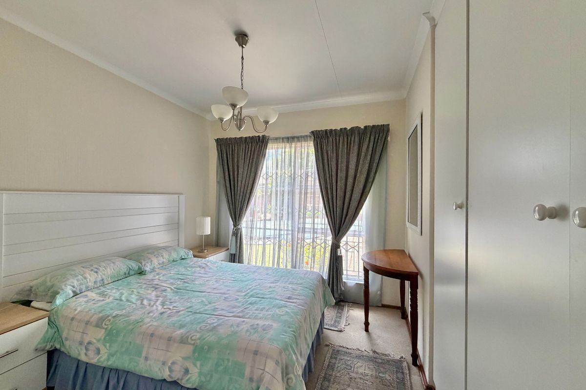 A well-lit bedroom featuring built-in cupboards, neutral wall finishes, and a window fitted with security bars, offering a functional and comfortable living space.