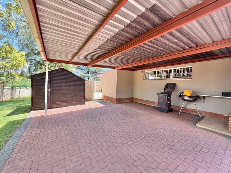 A covered carport area featuring brick paving, a corrugated metal roof, and an adjacent external storage shed.