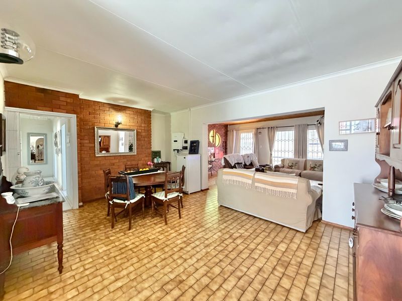Spacious open-plan living and dining area featuring a distinctive exposed brick wall, ceramic tile flooring, and direct access to adjacent living spaces.