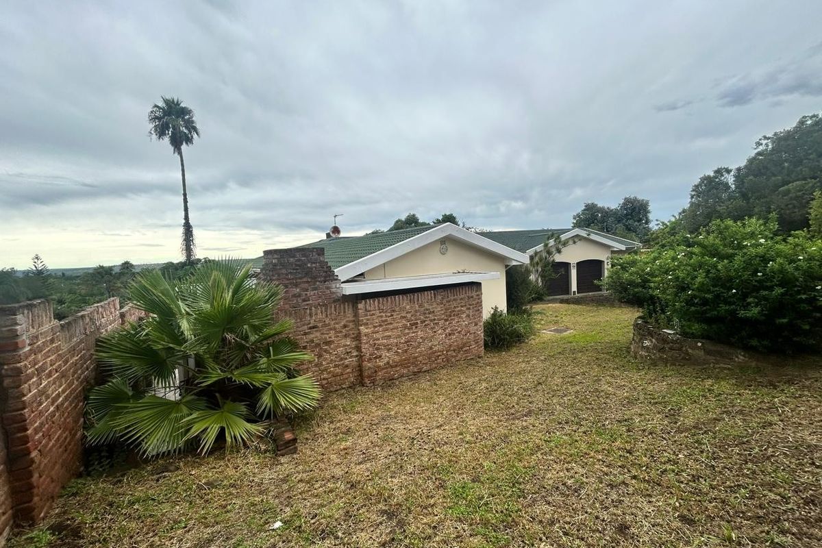 Rear view of the property featuring a brick boundary wall, tiled roof, and double garage access set within a large garden area.