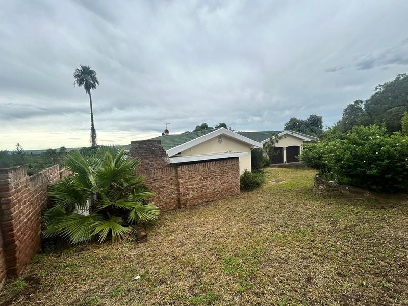 Rear view of the property featuring a brick boundary wall, tiled roof, and double garage access set within a large garden area.