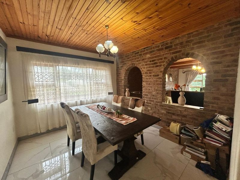 Dining room featuring a rustic timber ceiling, exposed brick wall with an archway, and modern tiled flooring.