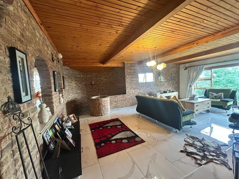 Spacious living room featuring exposed brick walls, a warm timber beam ceiling, and modern tiled flooring with an open-plan layout.