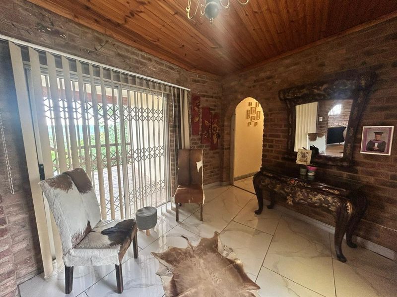Living room featuring exposed brick walls, timber ceiling, and tiled flooring, with a sliding door leading to an outdoor area.