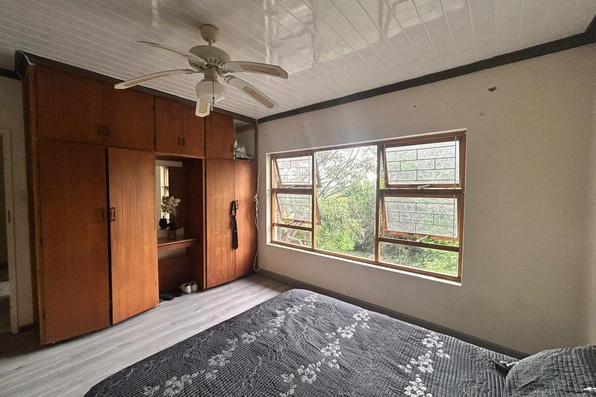 Bedroom featuring built-in wooden cabinetry, laminate flooring, and a ceiling fan, with large windows providing natural light and garden views.