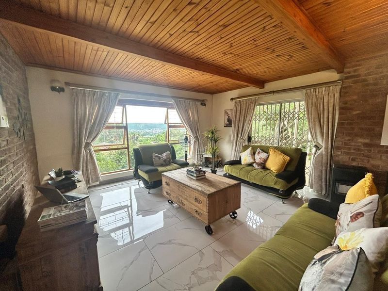 Spacious living room featuring exposed timber beam ceilings, rustic brick walls, and modern marble-look floor tiles with large windows offering scenic views.