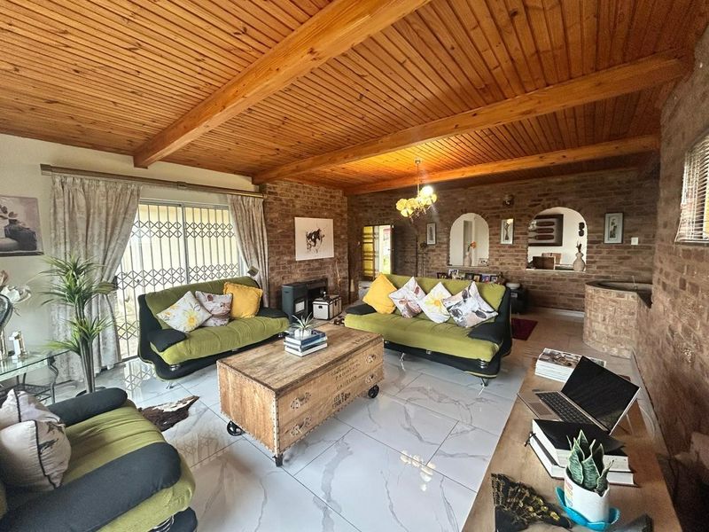 Spacious living room featuring exposed brick walls, a warm timber beam ceiling, and modern tiled flooring with an open-plan feel.