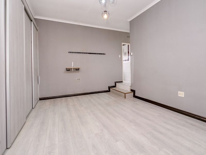 A clean, empty bedroom featuring light-toned laminate flooring, a built-in sliding wardrobe, and a small raised step leading to an adjacent area.