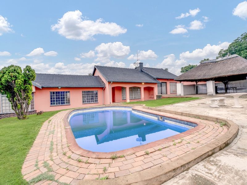 Rear garden area featuring a swimming pool with brick surround and a separate thatched lapa structure.