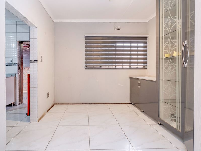 A bright, tiled kitchen area featuring built-in cabinetry and a window with blinds, offering a clean, neutral space ready for final finishing touches.