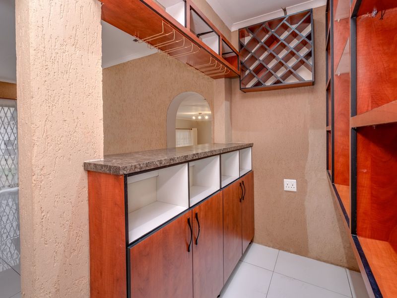 A dedicated bar area featuring built-in wooden cabinetry, a wine rack, glassware storage, and a laminate countertop, finished with tiled flooring.