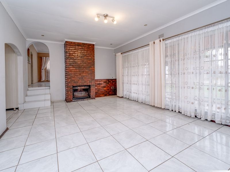 Spacious living room featuring tiled flooring, a prominent brick fireplace, and an arched entryway leading to adjacent living areas.
