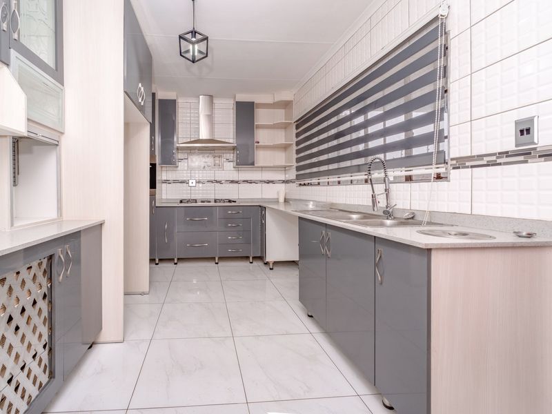 Modern kitchen featuring grey and light wood cabinetry, stone countertops, stainless steel sink, gas hob, extractor fan, and tiled finishes throughout.