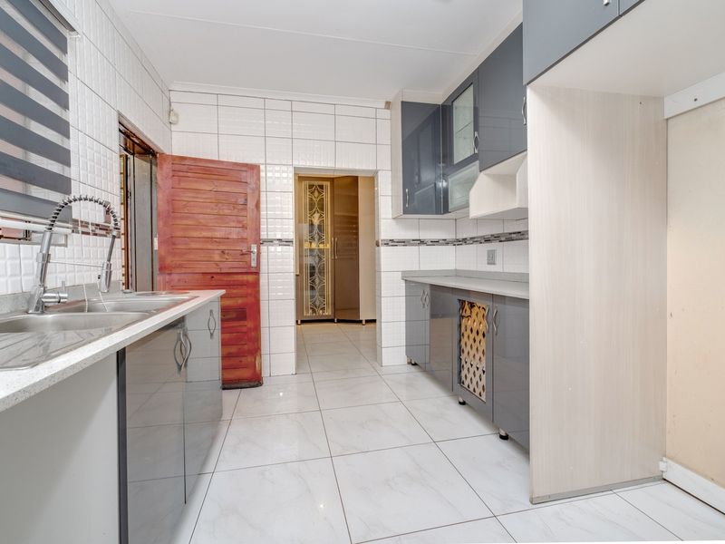 A functional kitchen featuring modern grey cabinetry, tiled walls and flooring, and a double sink with a contemporary gooseneck faucet.