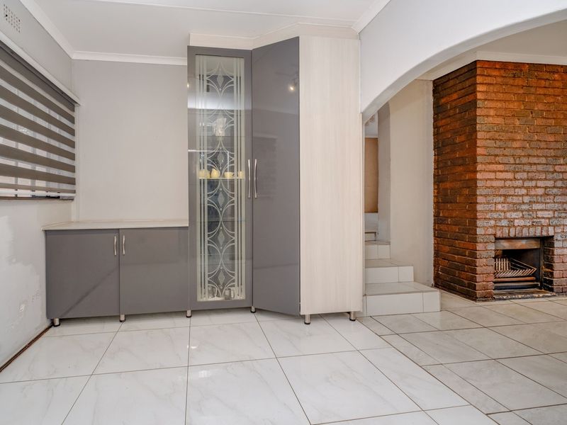 Living area featuring tiled flooring, a prominent brick fireplace, and modern built-in cabinetry with glass display detailing.
