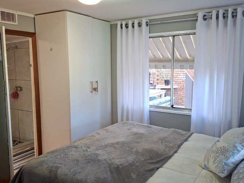 A functional bedroom featuring a built-in wardrobe, natural light through a sliding window, and direct access to an en-suite bathroom.