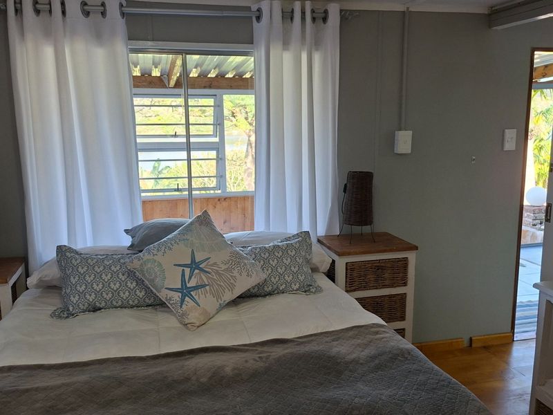 A bedroom featuring timber flooring and a sliding window with views, finished with neutral wall tones and exposed electrical conduit.