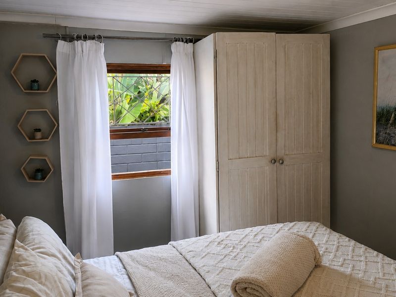 A cozy bedroom featuring a timber-framed window, neutral wall tones, and a classic tongue-and-groove ceiling finish.